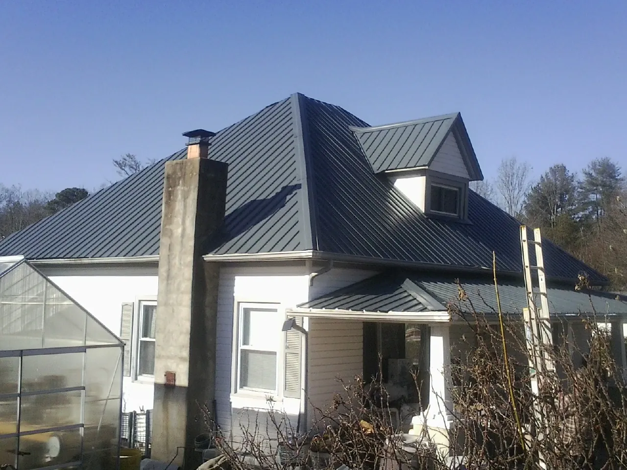 Dark blue standing seam metal roof on a white farmhouse with dormer — Slate & Tile Roof Repair by Roofing Brothers in Rutherford College
