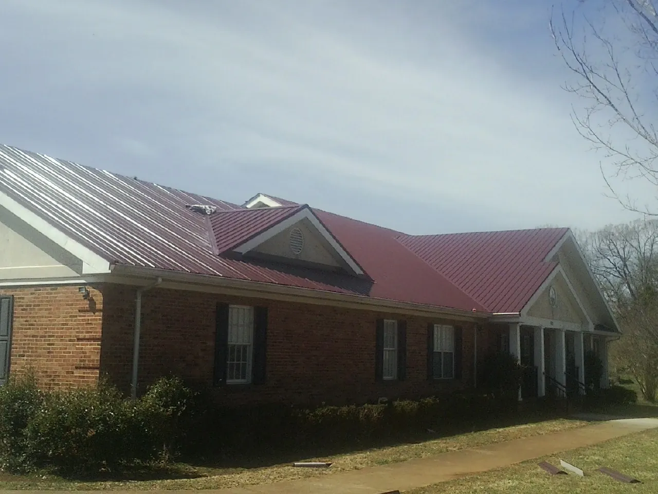 Red metal roof with gabled entries on a long brick building, from a Hail Damage Roof Repair job in Rutherford College