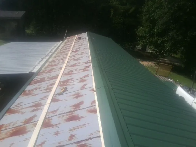 Old rusted panels beside newly installed green metal roofing — Wind Damage Roof Repair by Roofing Brothers in Rutherford College