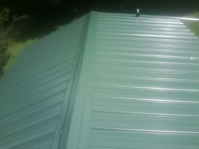New green metal panels meeting at the ridge of a roof — Flat Roof Repair work by our crew in Rutherford College