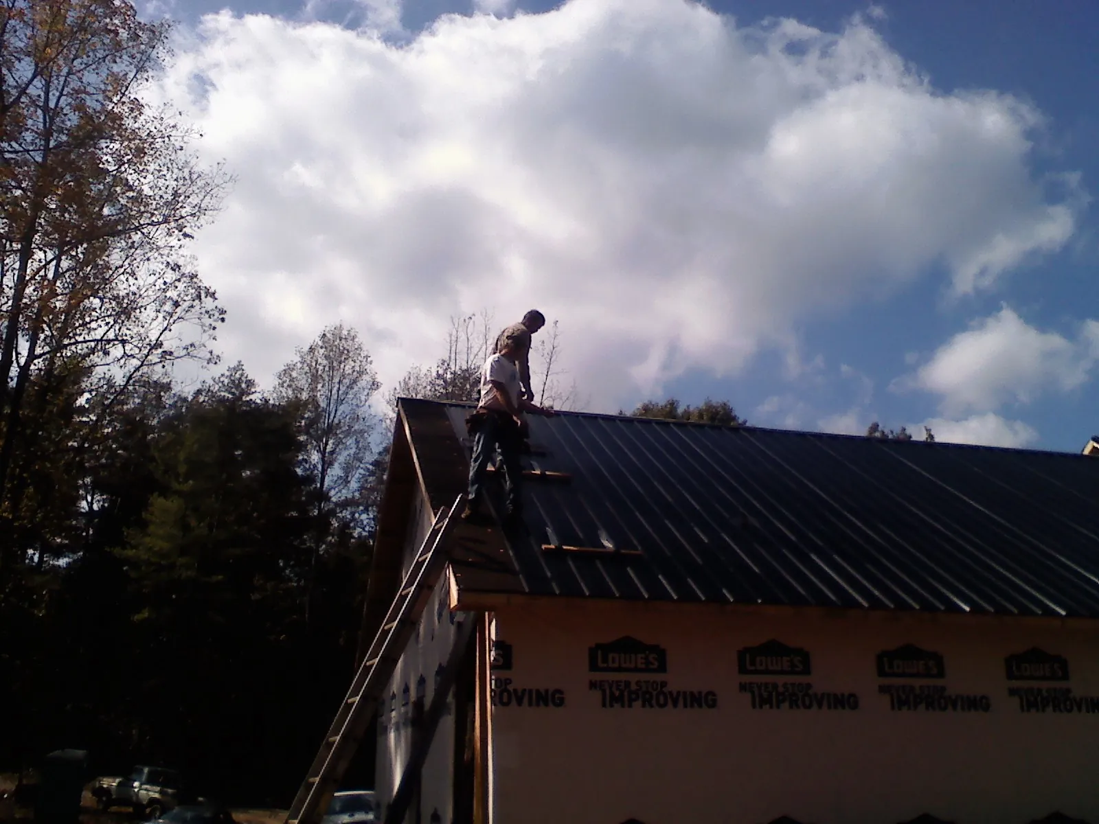 Roofer fastening dark metal panels high against a cloudy sky, from a Roof Inspection job in Rutherford College