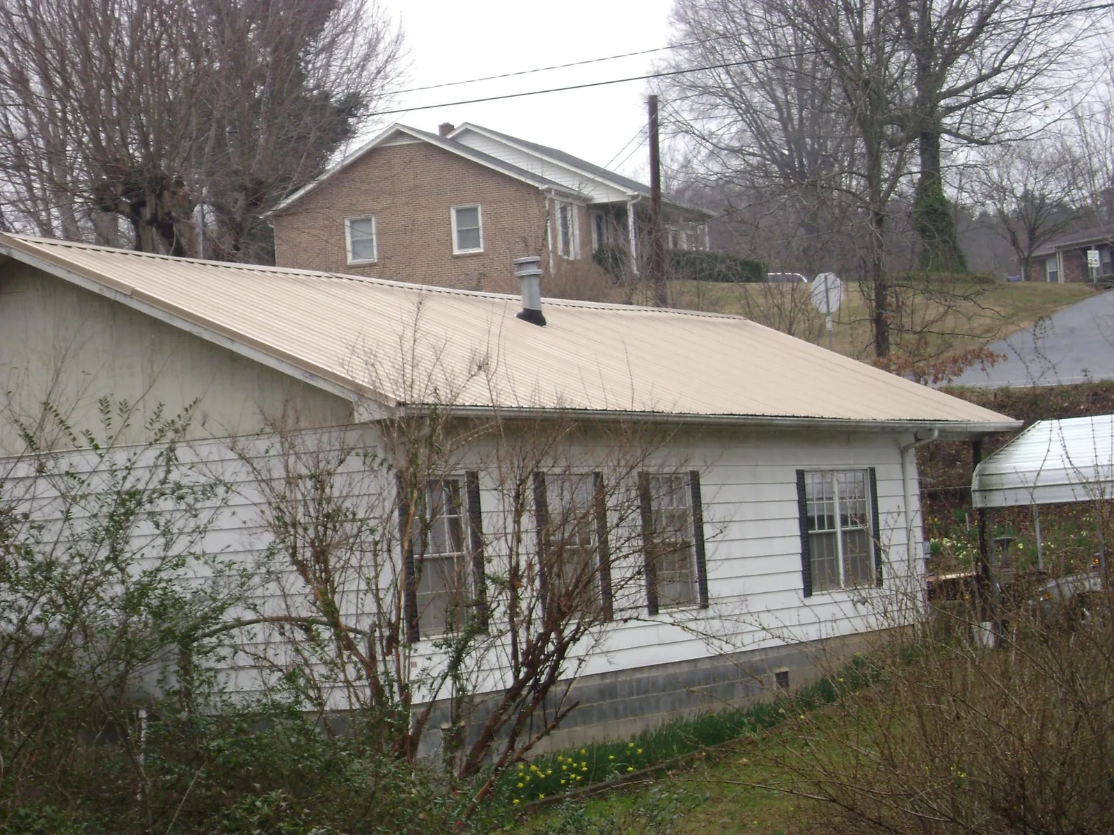 Tan metal roof on a white sided house set into a hillside — Commercial Roofing by Roofing Brothers in Rutherford College