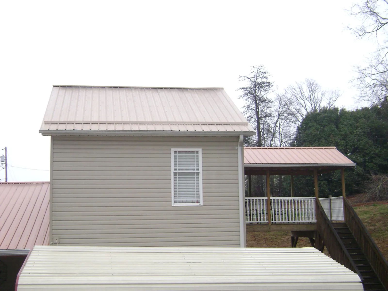 Tan metal roofs on a two story addition and attached porch, from a Roof Replacement job in Rutherford College